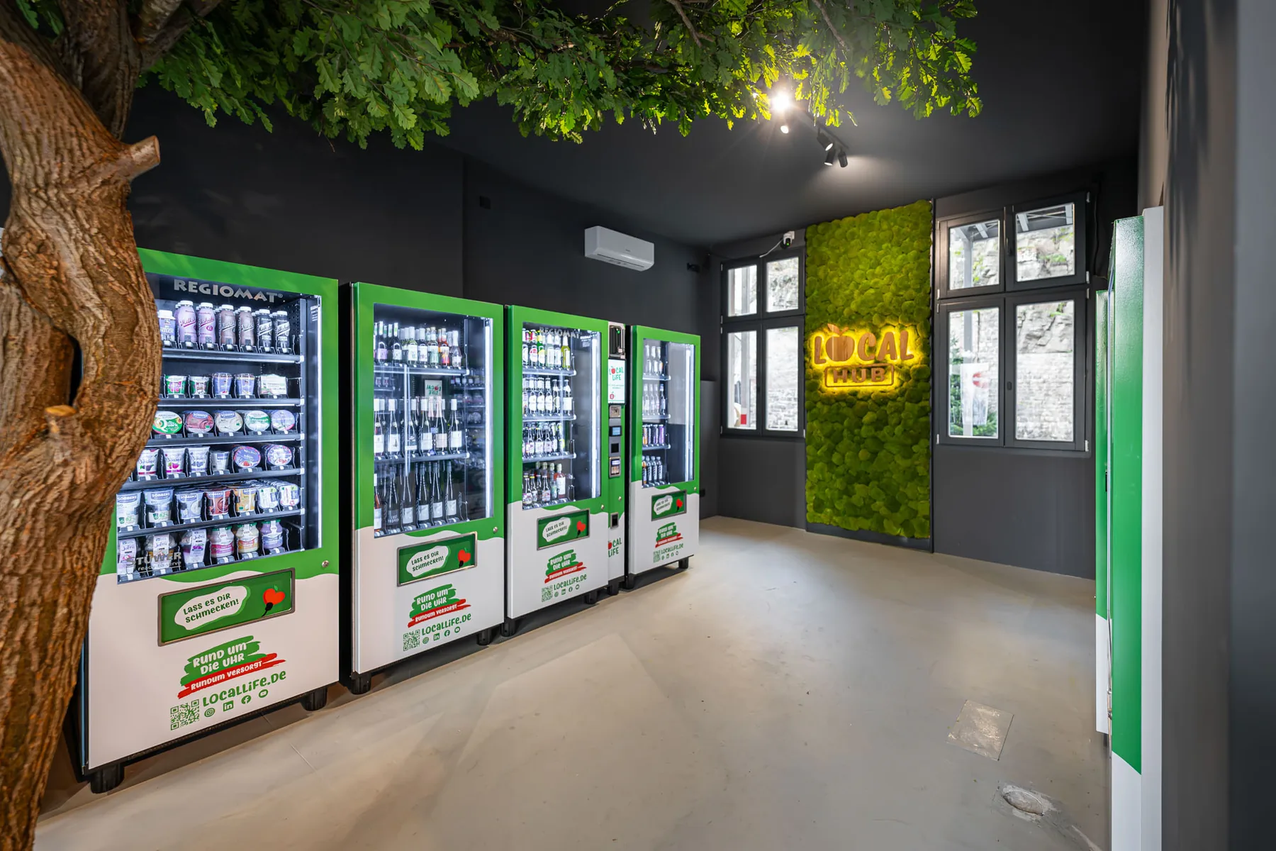 Innenansicht des Local Hub mit Automaten und Baum in der Raummitte