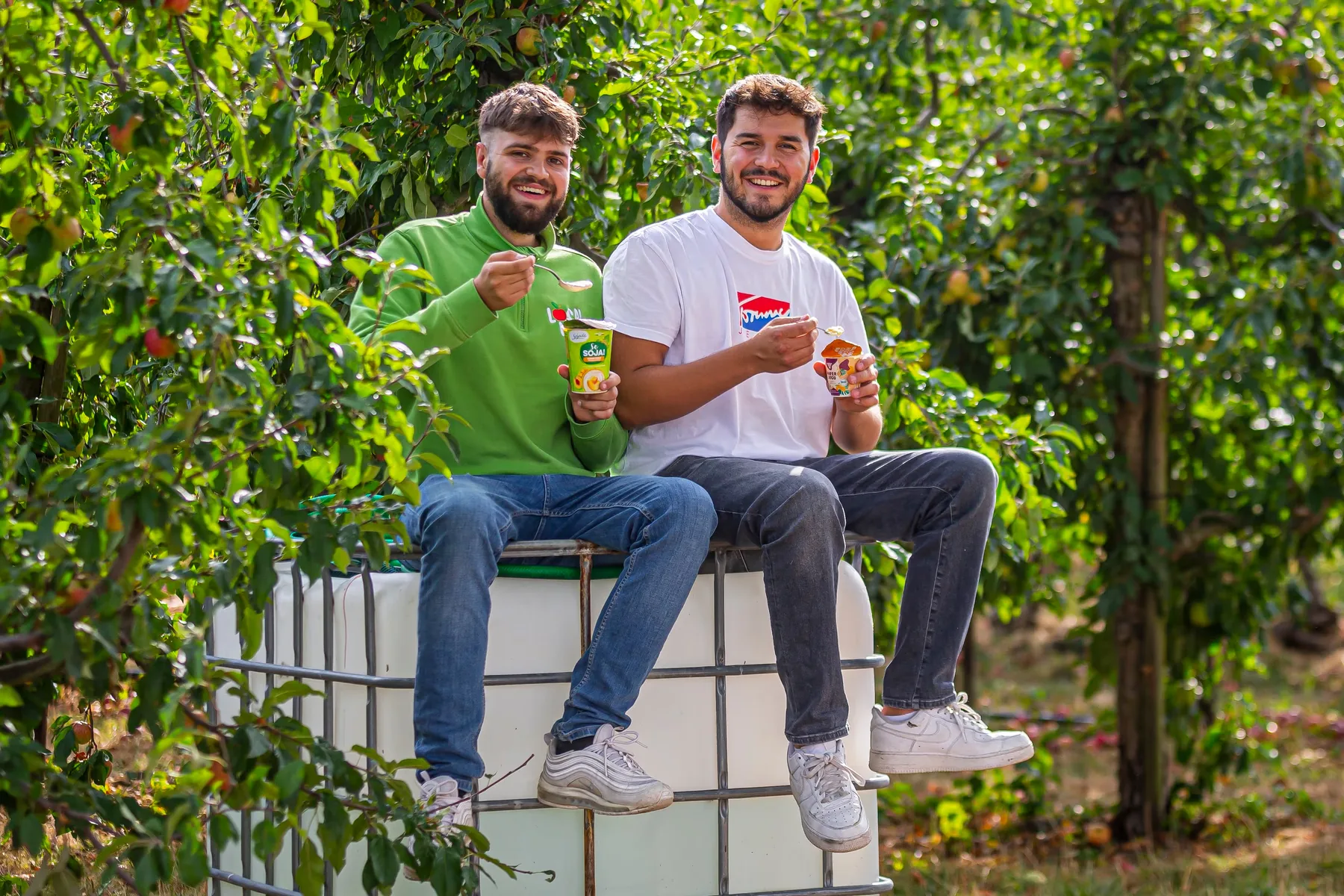 Valentin Steinbrenner mit einem Kollegen zwischen Obstbäumen, beide essen Joghurt aus dem Local Life Automaten